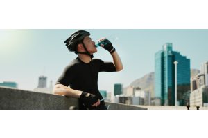 Ein Mann mit Fahrradhelm trinkt aus einer Wasserflasche.