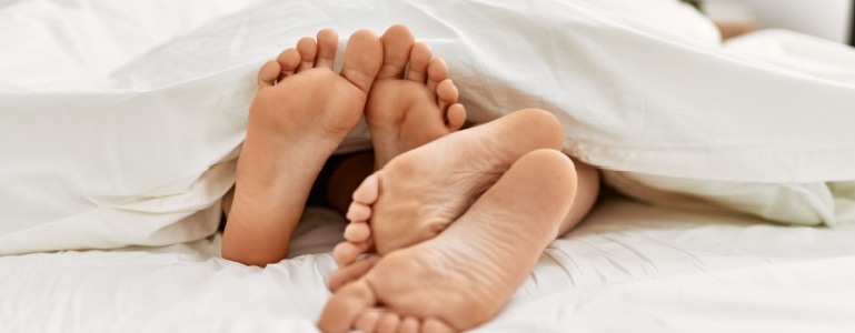 Füße eines Paares, die unter der Bettdecke hervorkommen
