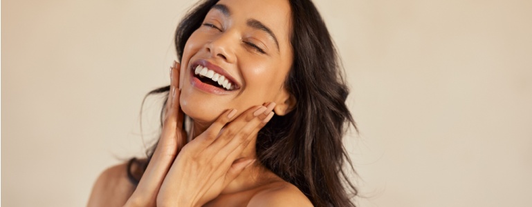 Eine lachende Frau berührt ihr Gesicht mit den Händen.