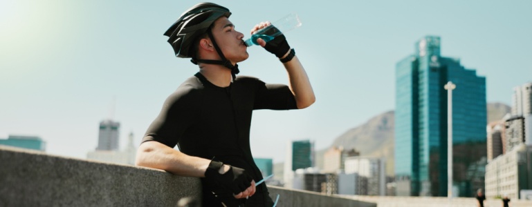 Ein Mann mit Fahrradhelm trinkt aus einer Wasserflasche.