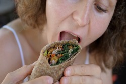 Eine Frau beißt in einen gesunden Wrap mit Gemüse und Hummus. Eine Frau beißt in einen gesunden Wrap mit Gemüse und Hummus.