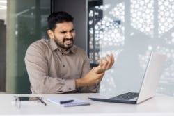 Mann hinter Laptop hält schmerzende Hand Mann hinter Laptop hält schmerzende Hand