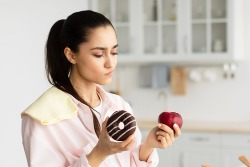 Eine Frau zögert zwischen einem Donut und einem Apfel. Eine Frau zögert zwischen einem Donut und einem Apfel.
