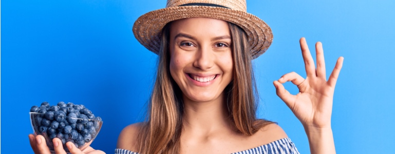 Glückliche, gesunde, junge Frau hält eine Schale Blaubeeren in der Hand