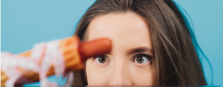 Frau betrachtet ein Hotdog mit einem Maßband