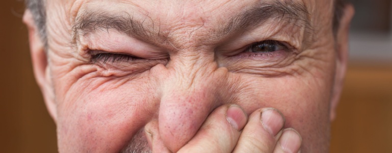 Ein alter Mann hält sich die Nase zu.