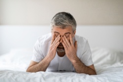 Der Mann liegt im Bett und reibt sich die Augen