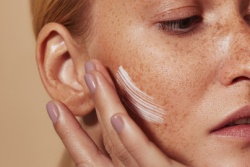 Die Frau tr&auml;gt Creme auf ihre Wange auf.