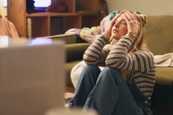 Eine Frau sitzt mit den Händen im Haar an die Couch gelehnt. Eine Frau sitzt mit den Händen im Haar an die Couch gelehnt.