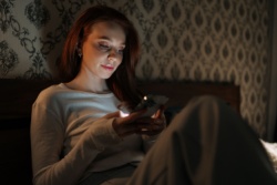 Frau scrollt im Bett auf ihrem Handy