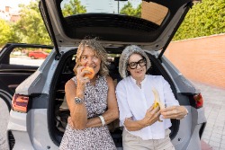 Zwei erwachsene Frauen essen im Auto ein St&uuml;ck Obst.