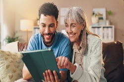 Eine lachende Frau sitzt mit einem jungen Mann zusammen und benutzt ein Tablet.